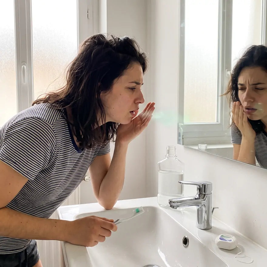 Dans la salle de bain, une femme vérifie son haleine dans sa paume, brosse à dents à la main, malgré le bain de bouche